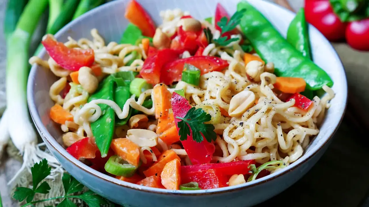 Schüssel mit Nudeln, Erdnüssen, Zuckerschoten, Karotten und Paprika. Ein leckeres Asia Salat Rezept.