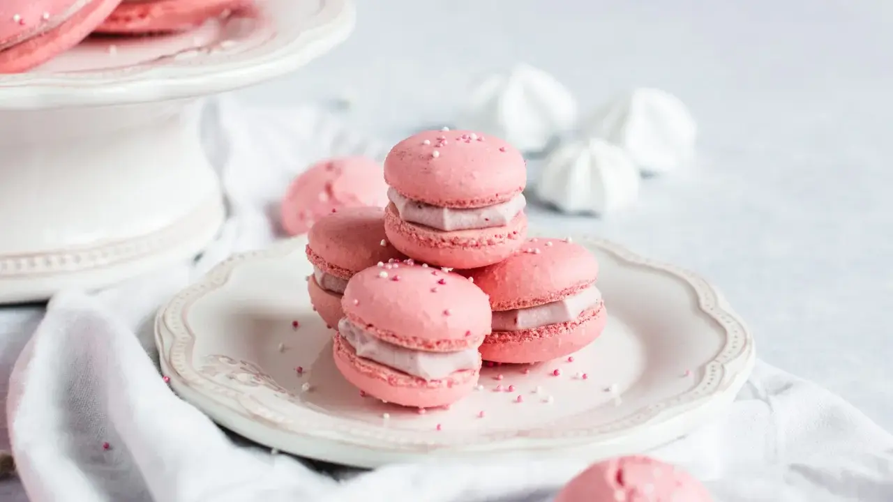 Rosa Macarons mit Himbeer-Ganache-Füllung, bestreut mit Zuckerperlen, auf einem Teller.