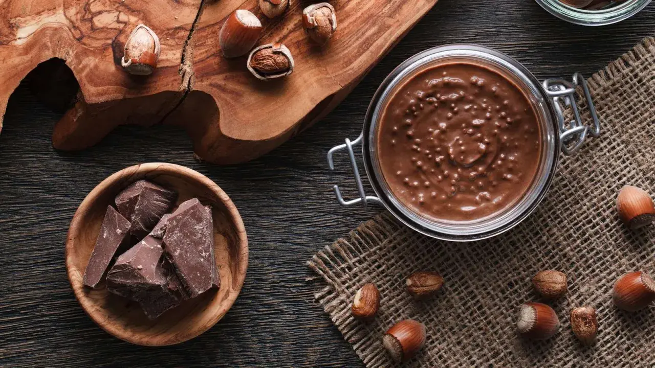 Zutaten für Nuss-Nougat-Creme selber machen: Haselnüsse, Schokolade und ein Glas voller Genuss.