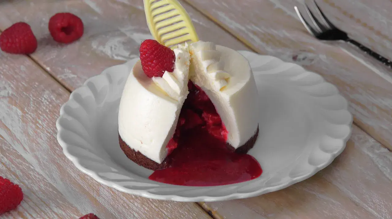 Ausgefallene Desserts zum Vorbereiten: Ein cremiges Dessert mit Himbeersauce und frischer Himbeere, dekoriert mit einem gelben Schokoladen-Detail.