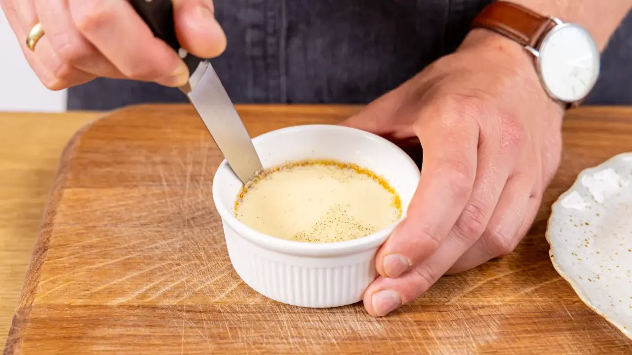 Ein Messer löst den Rand eines cremigen Flan Puddings in einer weißen Keramikschale.