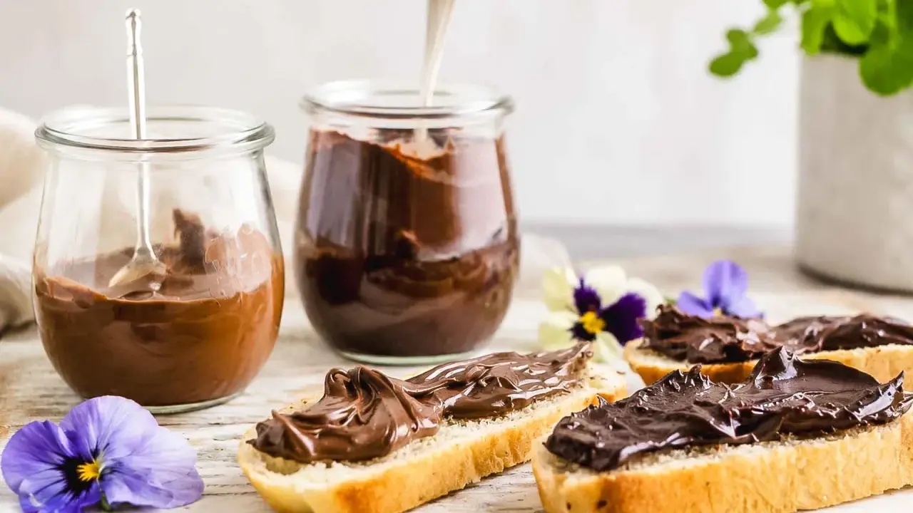 Zwei Gläser mit schoko creme, daneben Brotscheiben, üppig bestrichen mit der cremigen Schoko-Leckerei, verziert mit Veilchen.