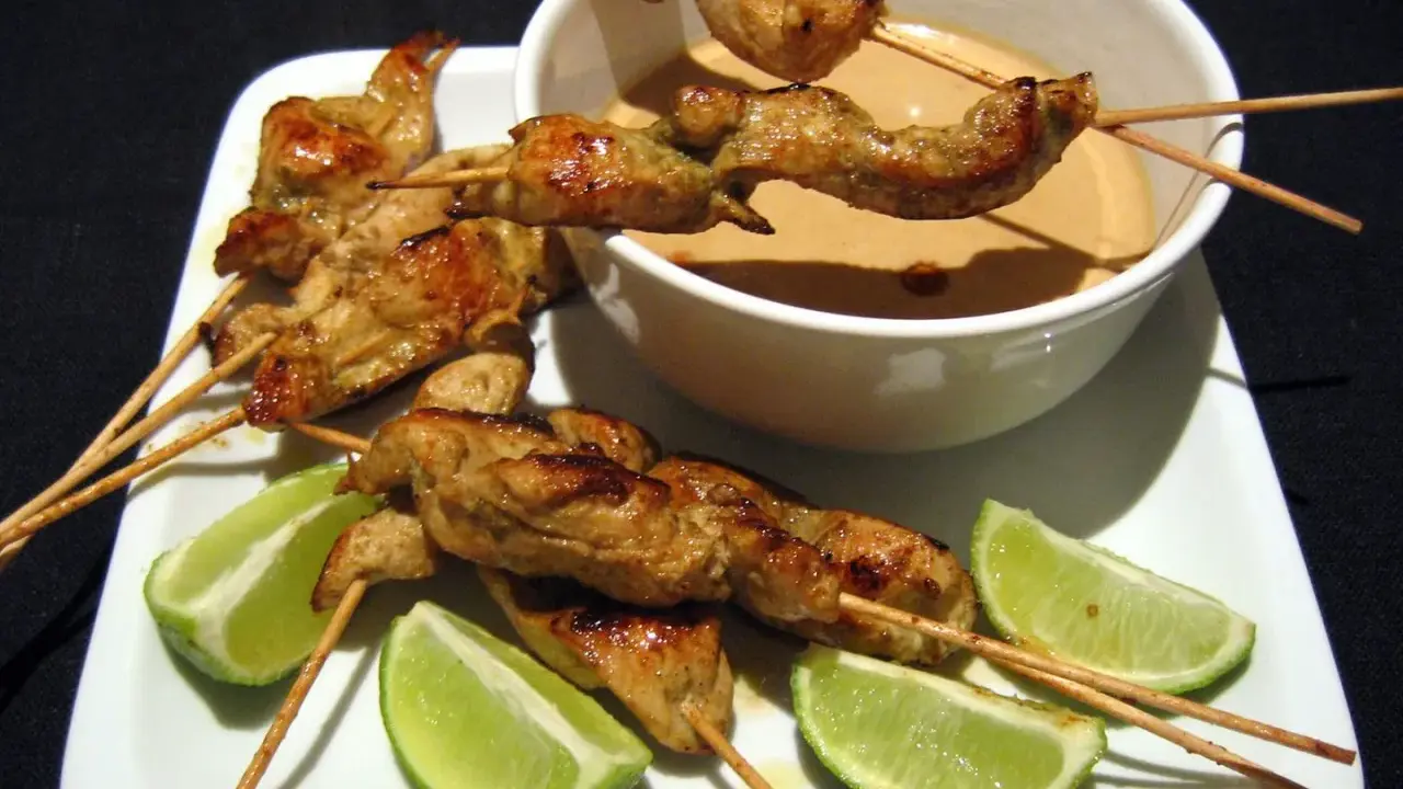 Saftige sate spiesse mit Erdnusssauce und Limettenspalten auf einem weißen Teller.