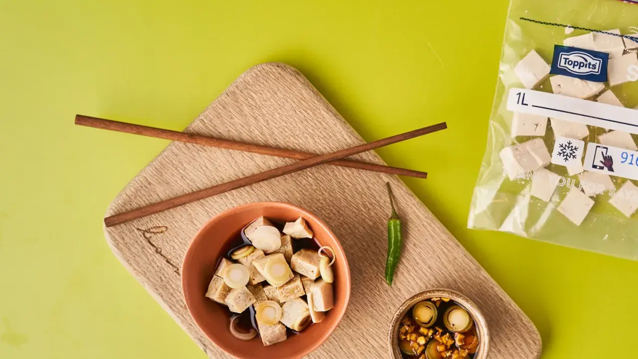 Vorbereitung für tofu einfrieren: gewürfelter Tofu in Schüssel mit Soße, Stäbchen, Chili und Beutel mit gefrorenem Tofu.
