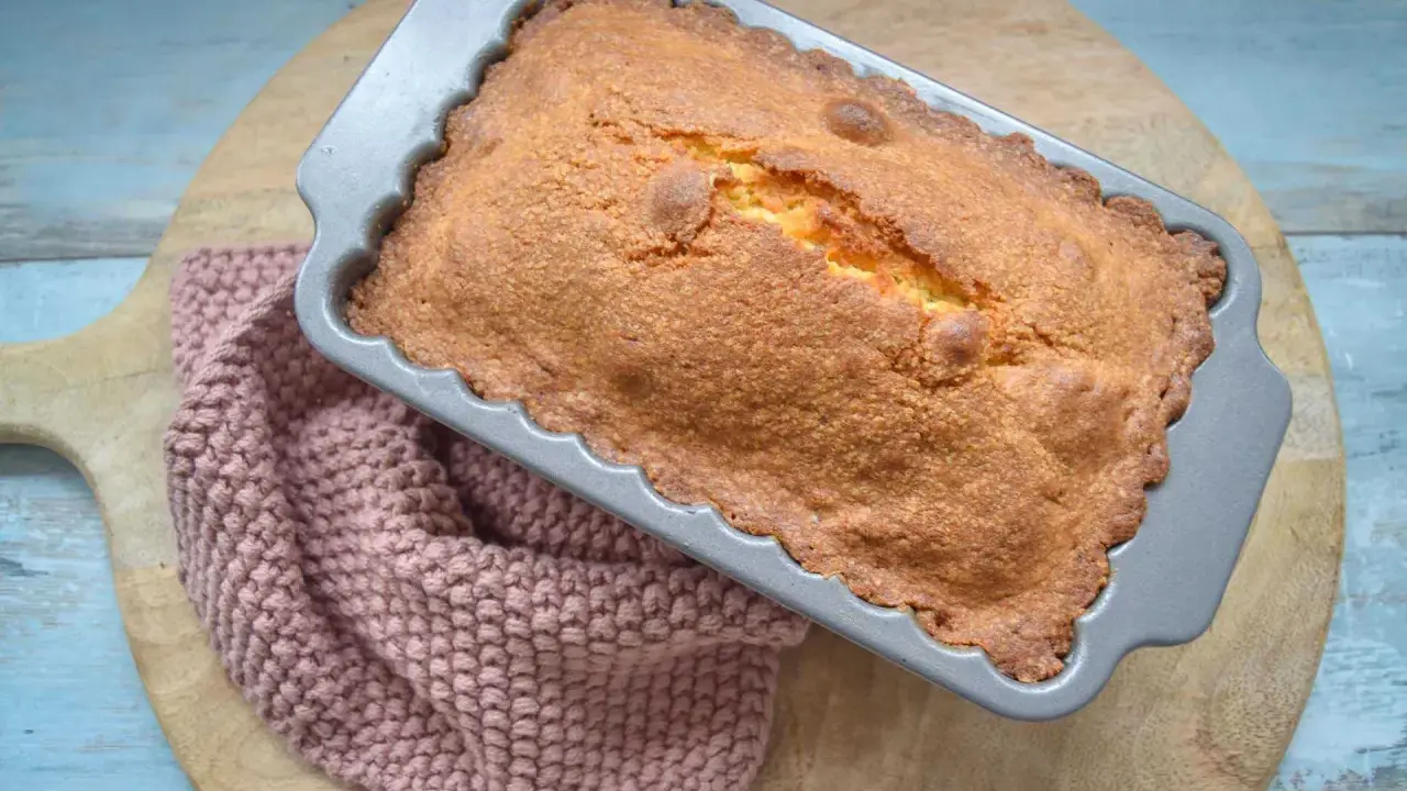 Frisch gebackener, goldbrauner quatre quarts in einer Kastenform, daneben ein rosafarbenes Stricktuch.