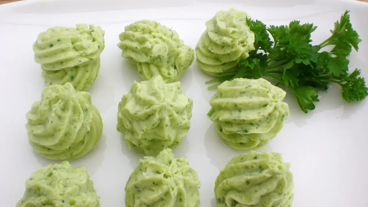 Grüne Kräuterbutter-Tuffs auf weißer Platte, perfekt für Ihre butter rezepte. Frische Petersilie daneben.