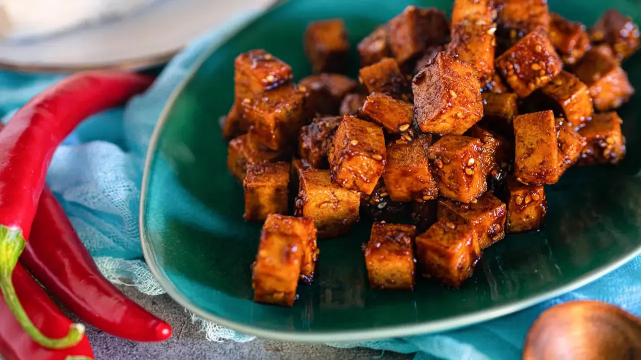 Würzig gebratene Tofuwürfel auf einem grünen Teller, daneben rote Chilis. So schmeckt Tofu!
