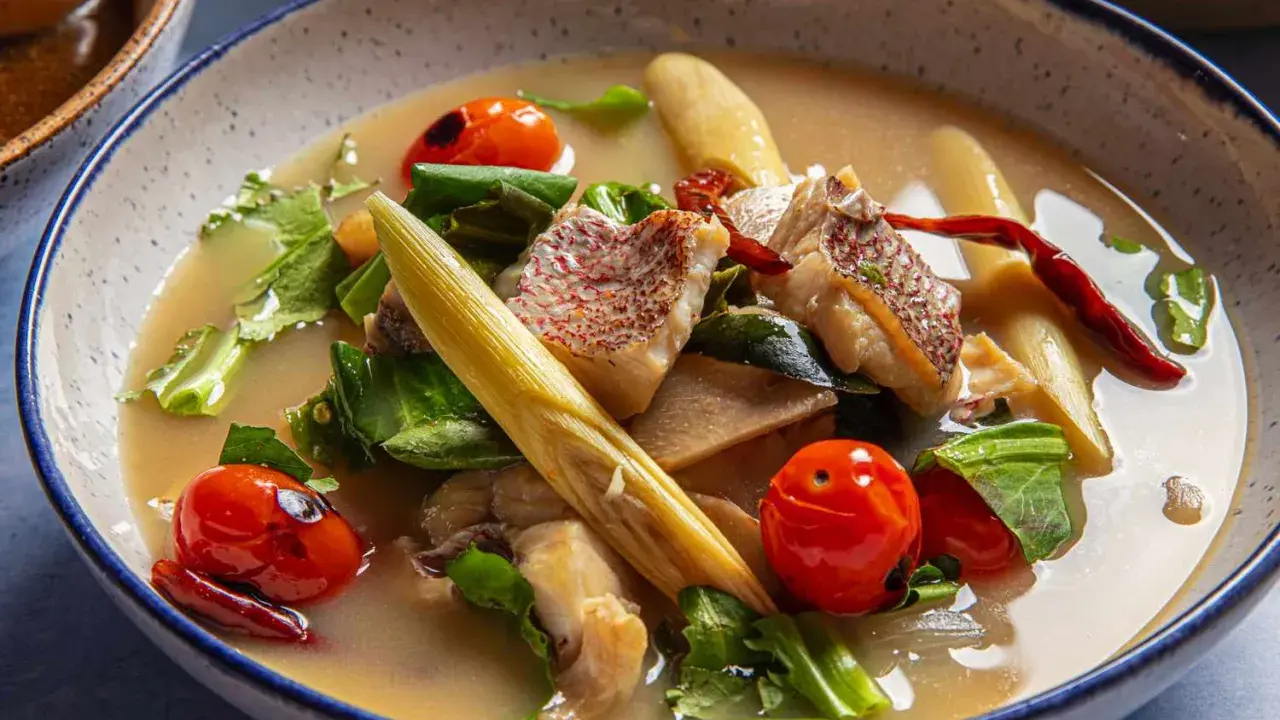 Eine dampfende Schüssel mit **thai Fischsuppe**, garniert mit Kirschtomaten, Kräutern und Zitronengras.