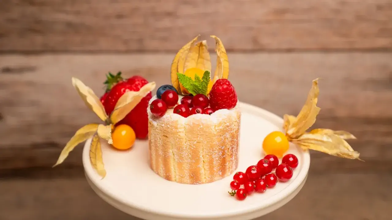 Ein kleiner Charlotte Kuchen, verziert mit frischen Beeren, Physalis und einem Hauch Puderzucker.