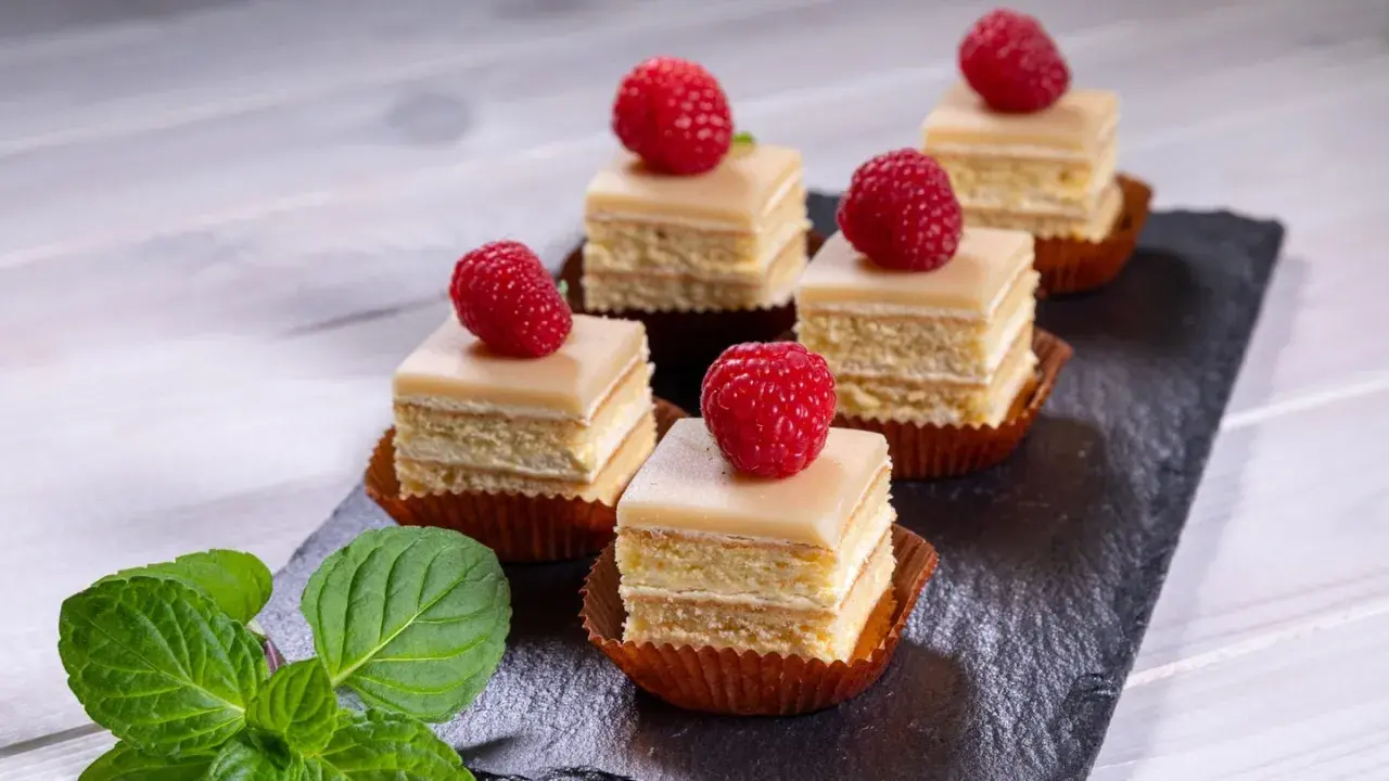 Sechs moderne Petit Fours mit Himbeeren und Minze auf einem Schieferbrett.