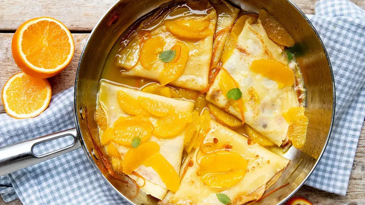 Crêpes Suzette im Originalrezept: zarte Pfannkuchen in Orangensauce mit frischen Orangenspalten und Minze garniert.