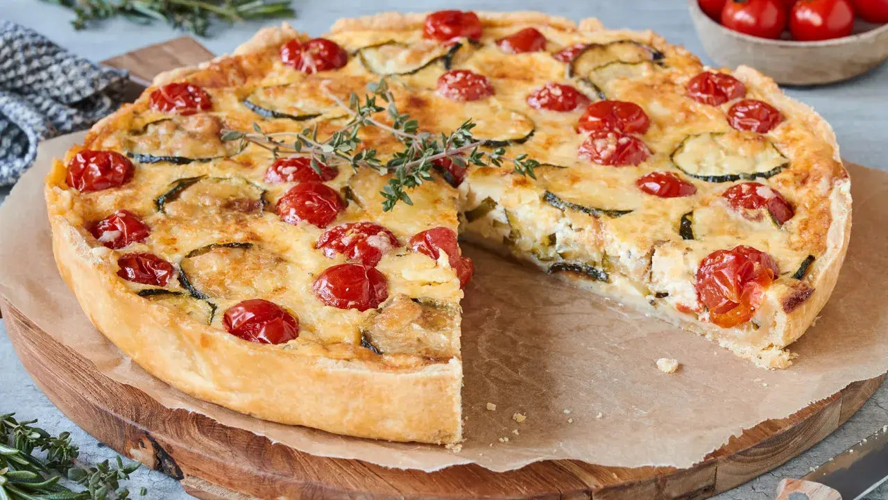 Eine köstliche, sommerliche Quiche mit Kirschtomaten und Zucchini, garniert mit frischem Thymian.