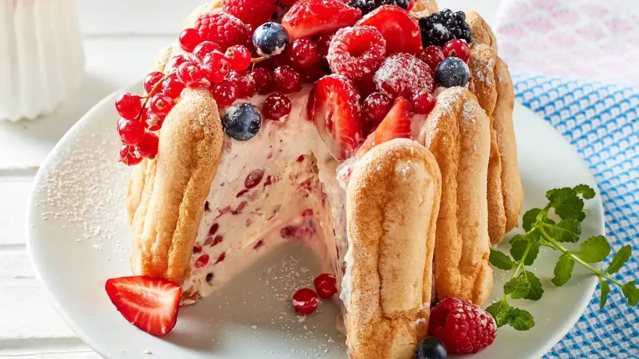 Eine köstliche Charlotte Torte, umhüllt von Löffelbiskuits und üppig belegt mit frischen Beeren wie Erdbeeren, Himbeeren und Johannisbeeren.