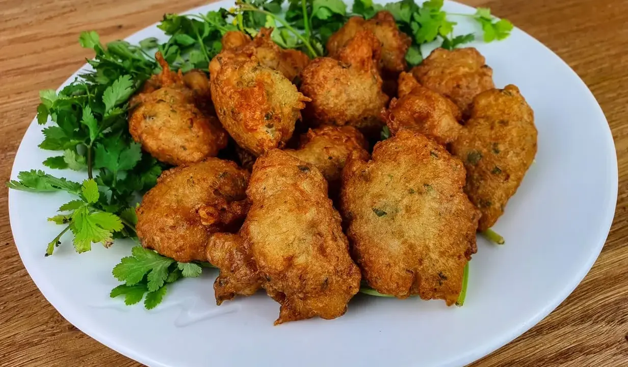 Knusprige Accras de Morue, goldbraun frittiert und mit frischer Petersilie garniert, auf einem weißen Teller.