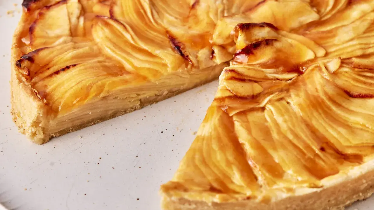 Eine köstliche Tarte au Pomme mit karamellisierten Apfelscheiben auf einem knusprigen Boden, auf einem rustikalen Teller.
