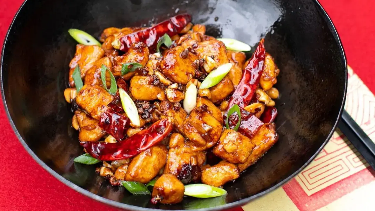 Ein köstliches Gericht mit asiatischen Rezepten mit Huhn, garniert mit Chilis und Frühlingszwiebeln in einer schwarzen Schüssel.