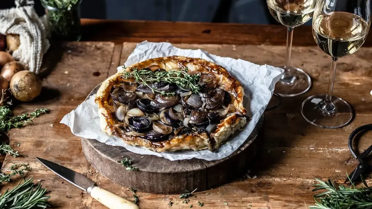 Herzhafte Tarte Tatin mit karamellisierten Zwiebeln und frischen Kräutern, serviert mit Weißwein.