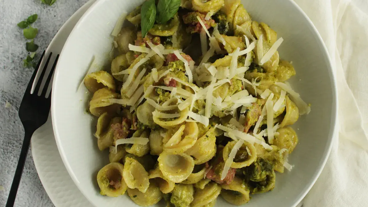 Orecchiette-Pasta mit grünem Pesto, Speck und geriebenem Parmesan. Ein köstliches Gericht, das zeigt, wie vielseitig Rezepte mit Pistazienmus sein können.