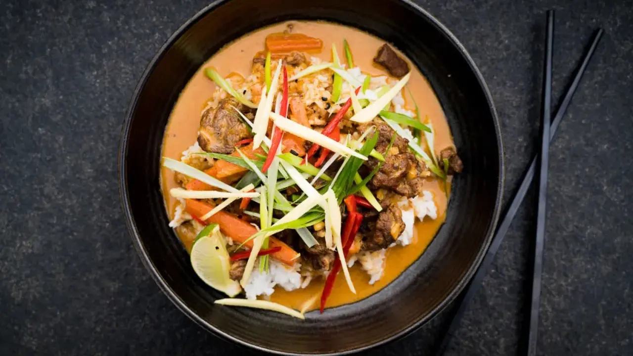 Ein aromatischer Thai Curry Rind mit Reis, Karotten und frischen Kräutern, garniert mit Limette.