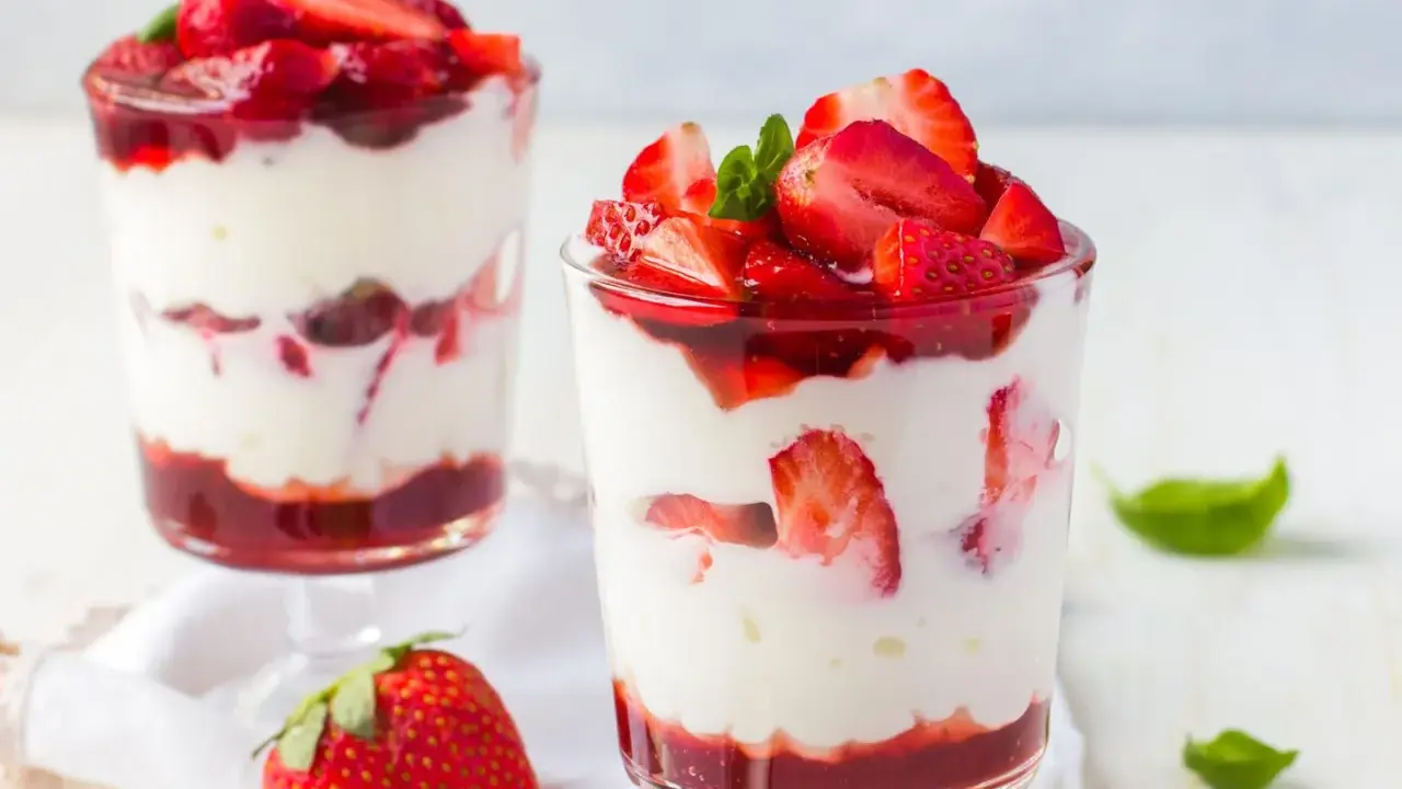 Zwei Gläser mit Erdbeer Mascarpone Creme, geschichtet mit frischen Erdbeeren und Erdbeersauce, garniert mit Minze.