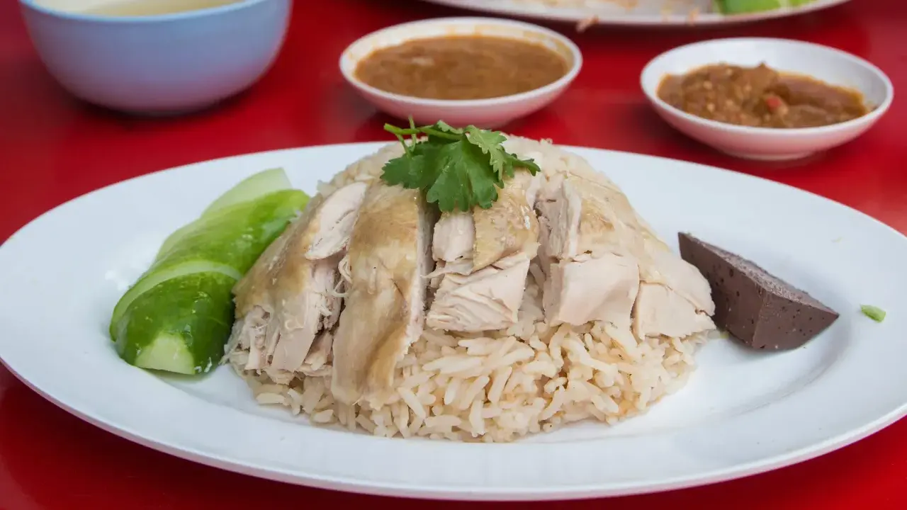 Khao Man Gai: gedämpfter Reis mit zartem Hühnchen, Gurkenscheiben und einer Blutwurstscheibe, garniert mit Koriander.