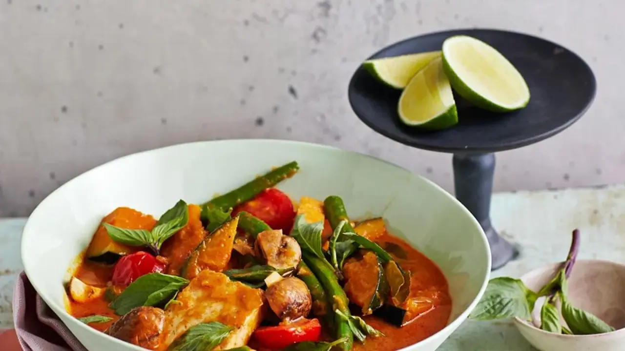 Ein köstliches Panang Curry mit Fisch, Kürbis, grünen Bohnen und Tomaten, garniert mit frischem Basilikum und Limettenspalten.