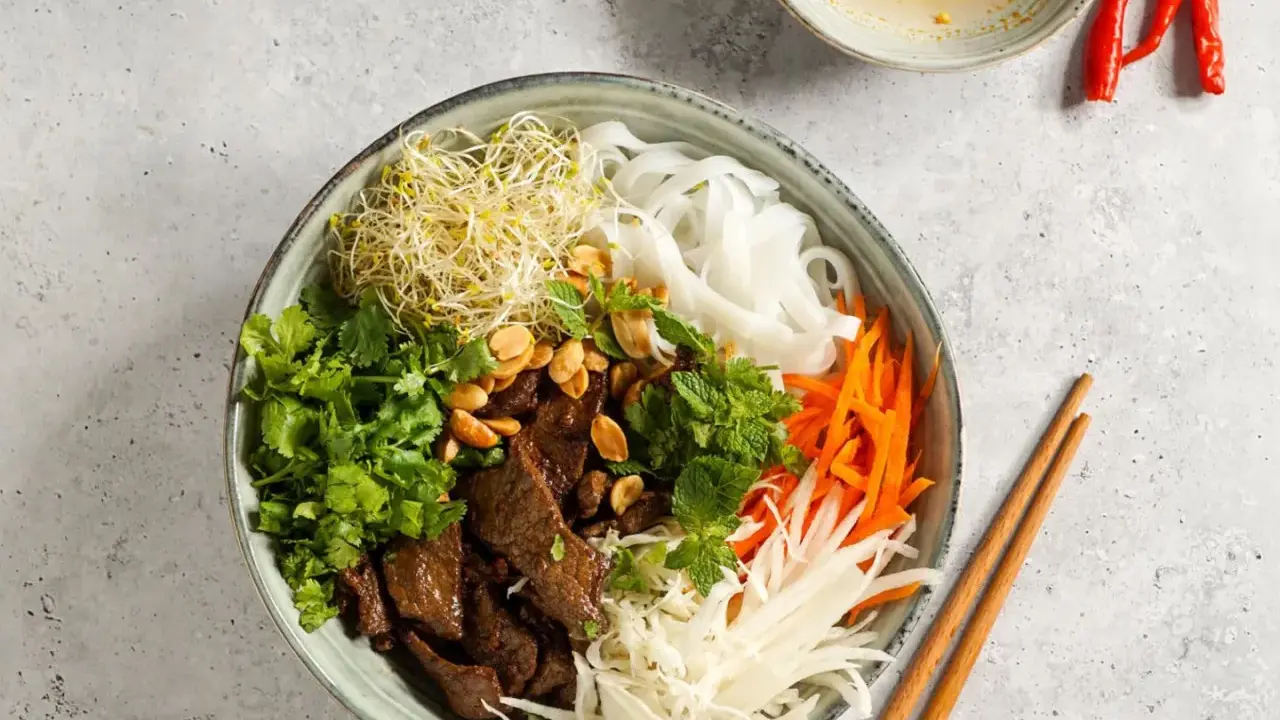 Bun bo nam bo: Reisnudeln, Rindfleisch, Sprossen, Karotten, Kohl und Kräuter in einer Schüssel, garniert mit Erdnüssen.