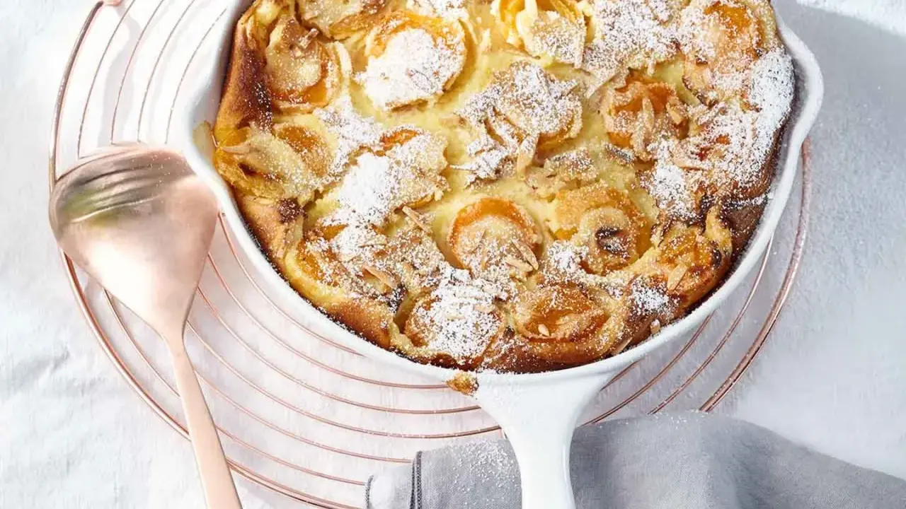 Ein goldbrauner Aprikosen Clafoutis, bestäubt mit Puderzucker und Mandelsplittern, wartet auf seine Verkostung.