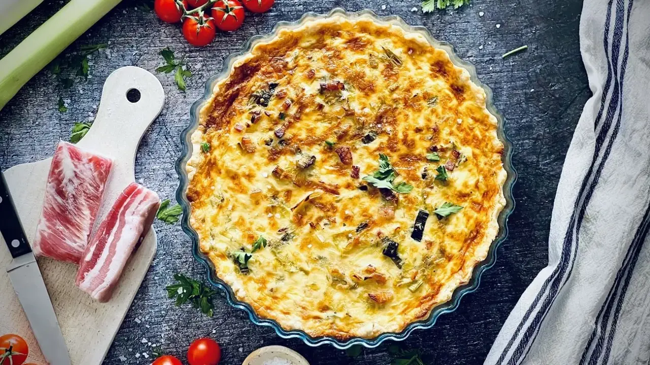 Herzhafte Quiche mit Speck und Lauch, perfekt für herzhafte Quiche Rezepte. Dazu frische Tomaten und Kräuter.