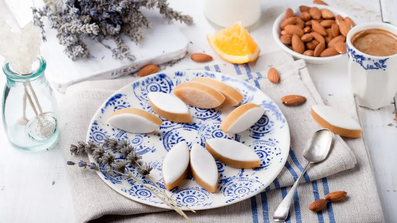 Calissons rezept: Süße Mandelkekse mit weißer Glasur auf blau-weißem Teller, garniert mit Lavendel und Mandeln.