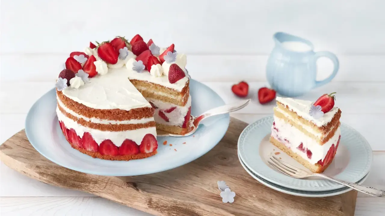 Eine köstliche Erdbeer Basilikum Torte mit frischen Erdbeeren und Sahne, ein Stück davon auf einem Teller.