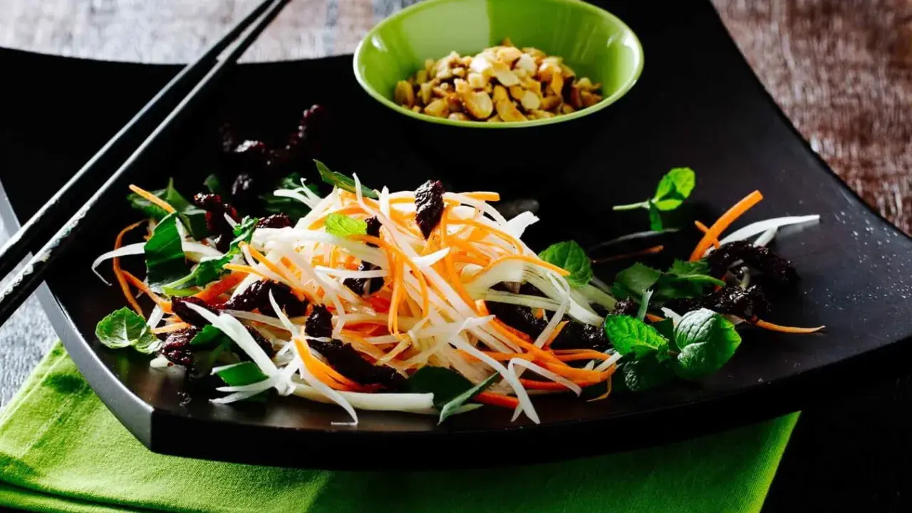 Ein bunter Papaya Salat vietnamesisch mit Karottenstreifen, Kräutern und gerösteten Erdnüssen.