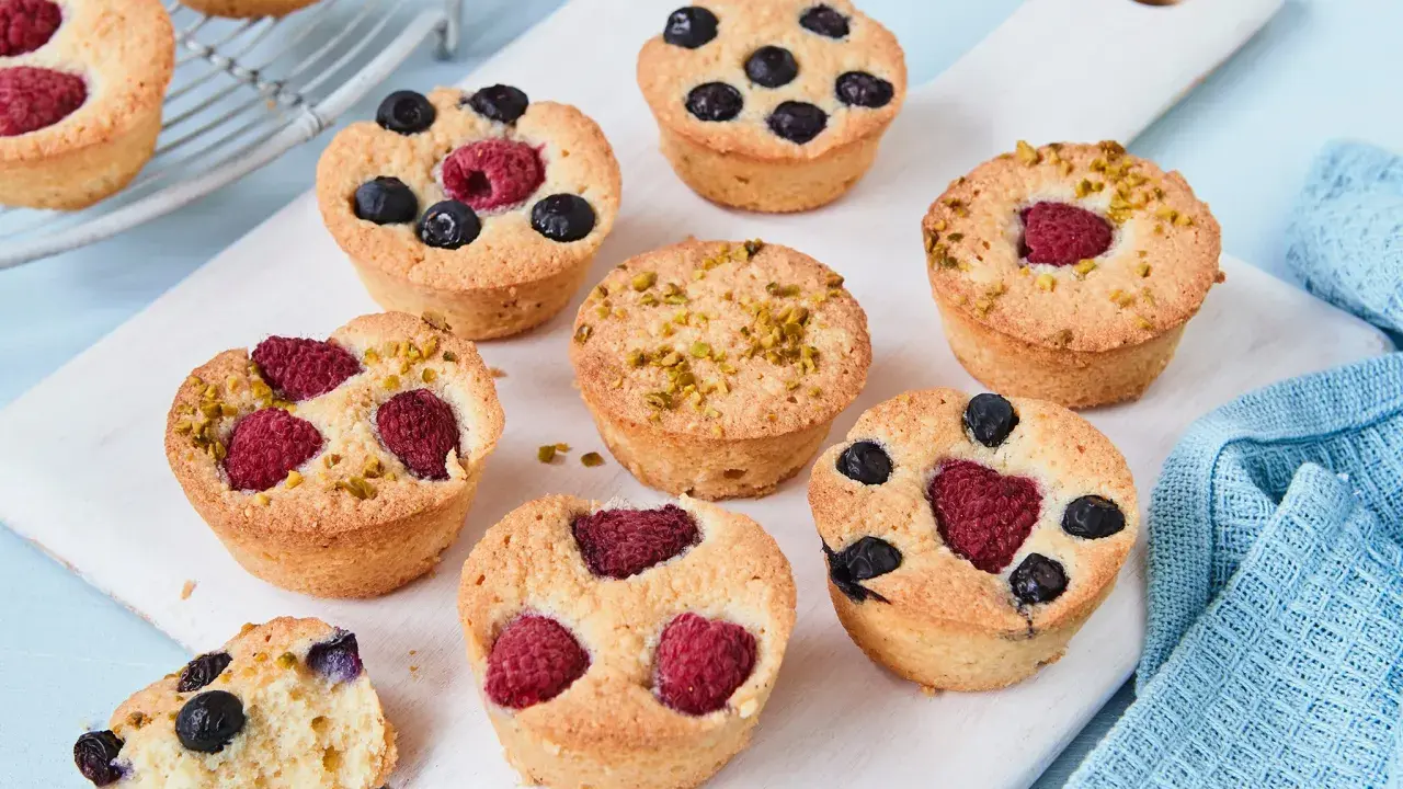 Kleine, goldbraune Financiers mit Himbeeren, Blaubeeren und Pistazien. Ein köstliches Financier Rezept zum Nachbacken.