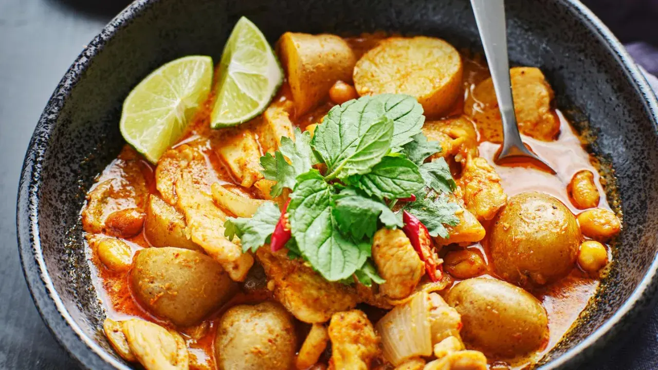 Ein köstliches Massaman Curry Rezept mit Hühnchen, Kartoffeln und Erdnüssen, garniert mit frischen Kräutern und Limettenspalten.