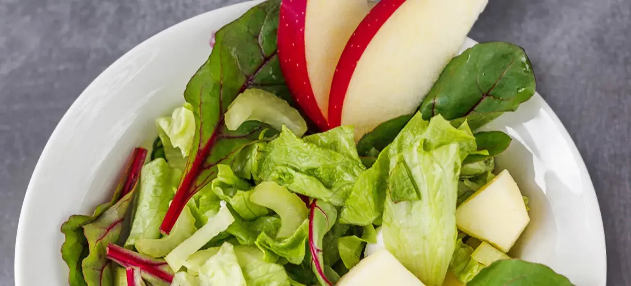 Frischer Romana Salat mit Apfelstücken und roten Mangoldblättern in einer weißen Schüssel.