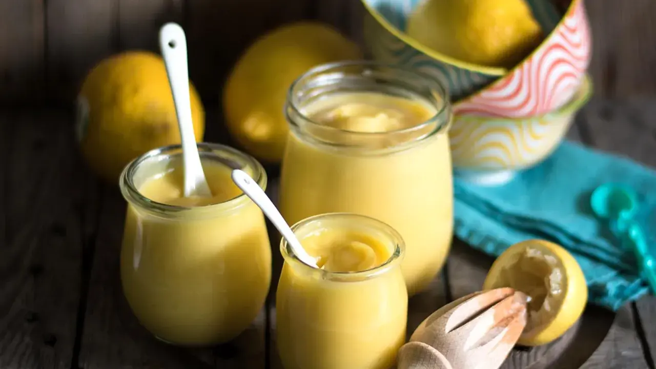 Leichte Zitronencreme im Thermomix zubereitet, serviert in Gläsern mit Löffeln, daneben frische Zitronen und ein Zitruspresse.
