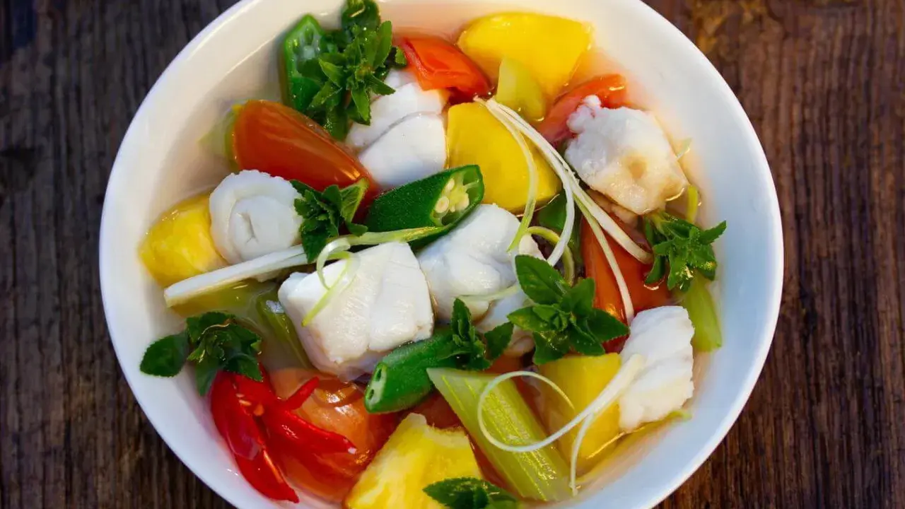 Ein Schüssel Canh Chua mit Fischstücken, Ananas, Tomaten, Okra und Kräutern.