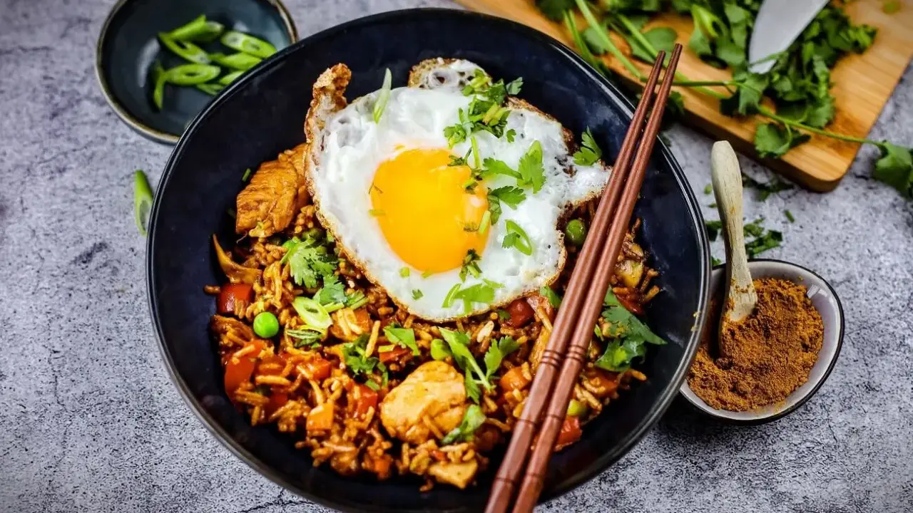 Was ist Nasi Goreng? Ein Teller mit gebratenem Reis, Hühnchen, Erbsen und einem Spiegelei, garniert mit Koriander und Frühlingszwiebeln.