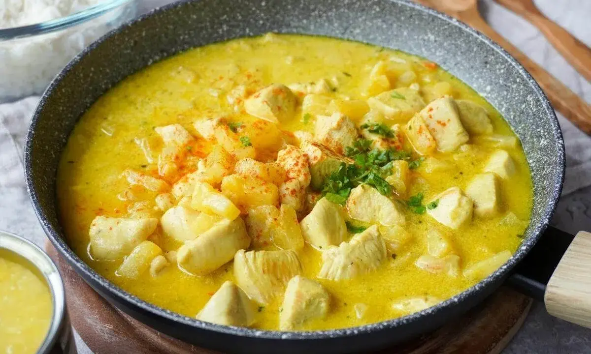 Ein köstlicher Curry mit Ananas und Hähnchenstücken in einer cremigen gelben Sauce, garniert mit Petersilie und Paprikapulver.