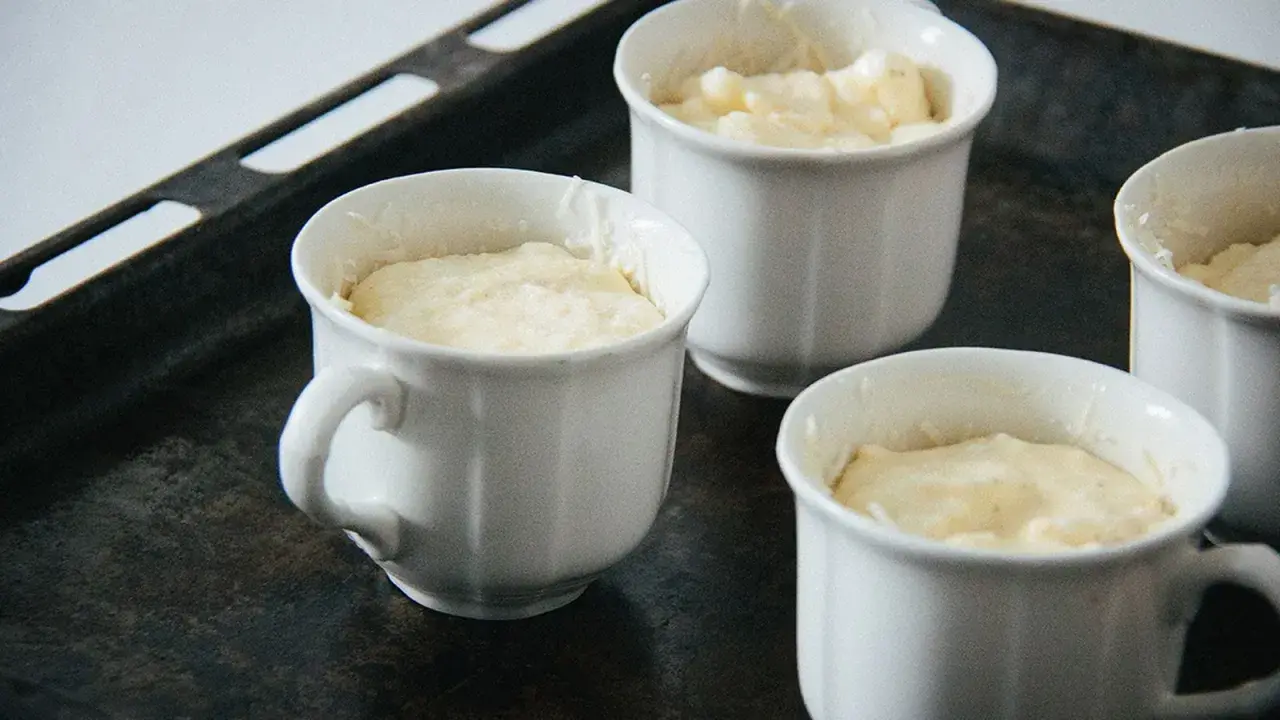 Vier weiße Förmchen mit luftiger Masse für ein Käsesoufflé stehen auf einem Backblech.