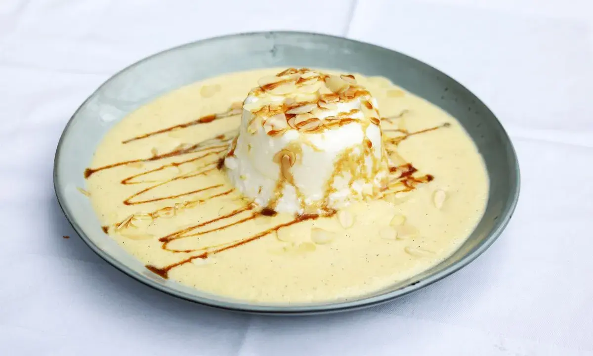 Ein leichtes, schwebendes Dessert aus Eischnee, umgeben von cremiger Vanillesauce, garniert mit Mandelsplittern und Karamell.