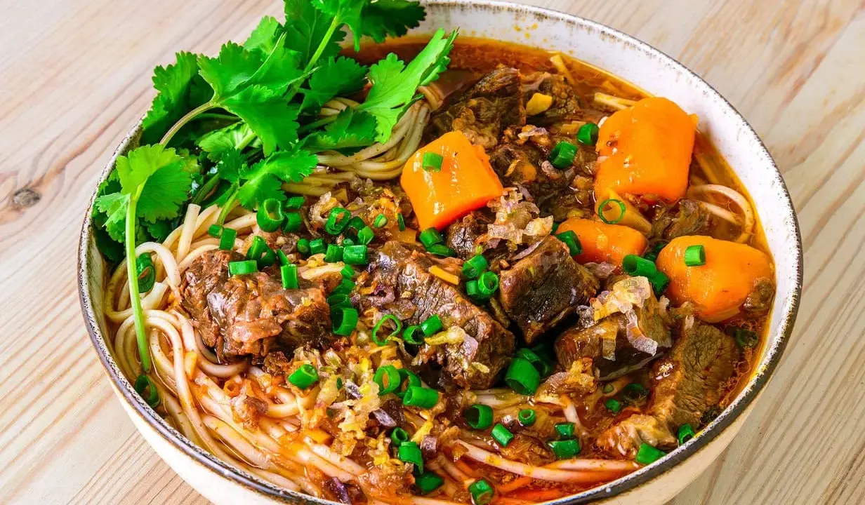 Herzhaftes Bo Kho mit zarten Rindfleischstücken, Karotten und Nudeln, garniert mit Koriander und Frühlingszwiebeln.