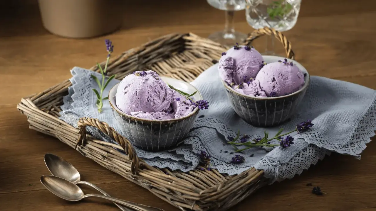 Zwei Schalen mit cremigem Lavendeleis, garniert mit Lavendelblüten, auf einem rustikalen Tablett.