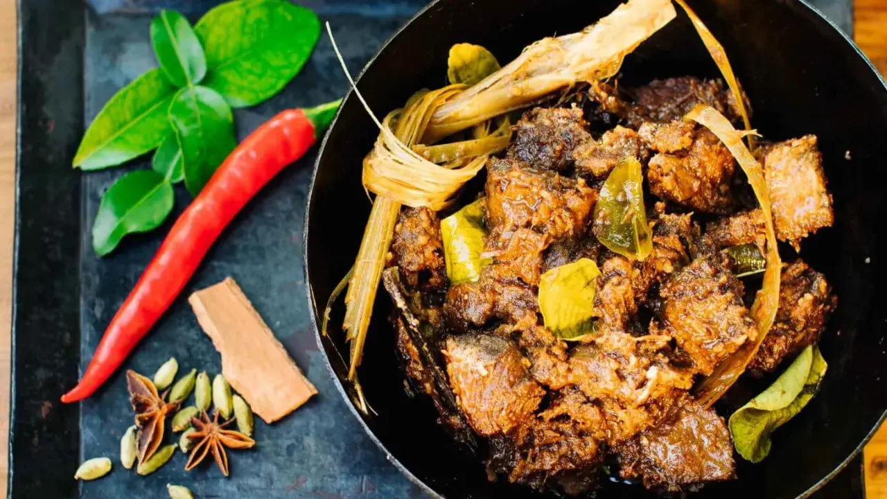Ein dampfender Topf mit würzigem Beef Rendang, daneben frische Kaffirlimettenblätter, Chili und Gewürze.