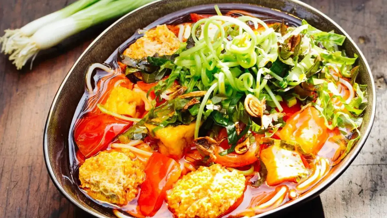 Herzhaftes Bun Rieu mit Tofu, Tomaten und frischen Kräutern, garniert mit Frühlingszwiebeln.