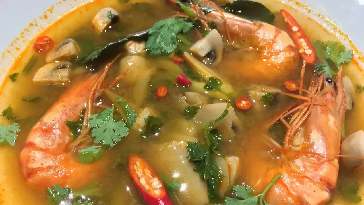 Eine dampfende Schüssel mit scharfer Thai Suppe, gefüllt mit Garnelen, Pilzen und Chili.
