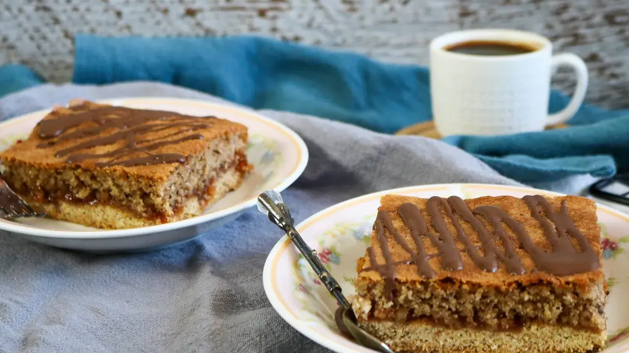 Zwei Stücke Blechkuchen mit Schokoladenglasur auf Tellern, perfekt, wenn man den Blechkuchen 3 Tage vorher backen möchte. Dazu eine Tasse Kaffee.