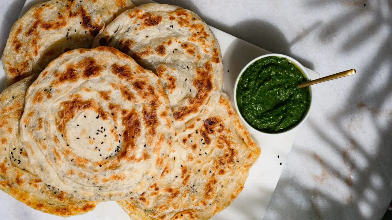 Fluffiger Roti Canai mit schwarzen Sesamkörnchen, daneben eine Schale mit grüner Chutney-Sauce.