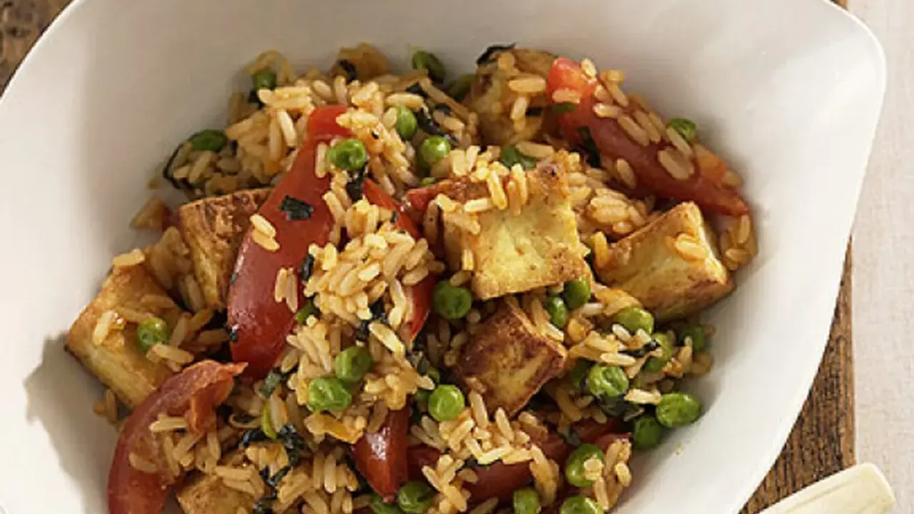 Herzhafter pilaw reis mit gebratenem Tofu, Erbsen und Tomatenstücken in einer weißen Schüssel.