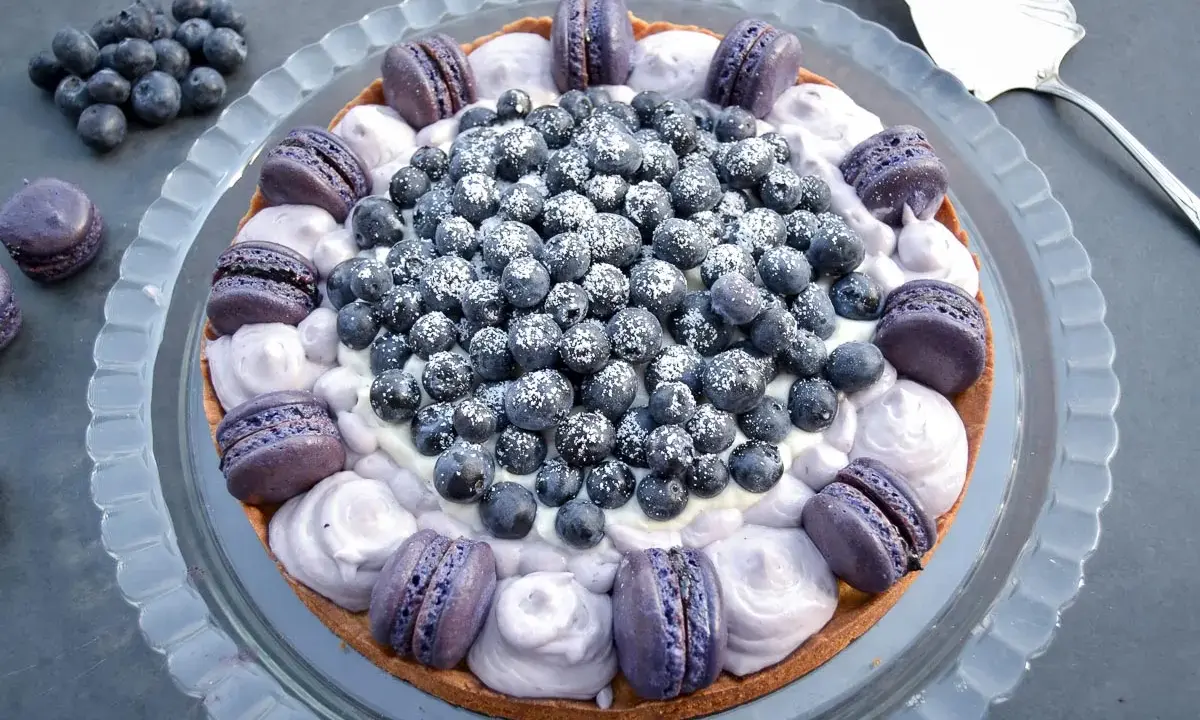 Eine Macaron Torte mit Blaubeeren und lila Macarons, bestäubt mit Puderzucker.